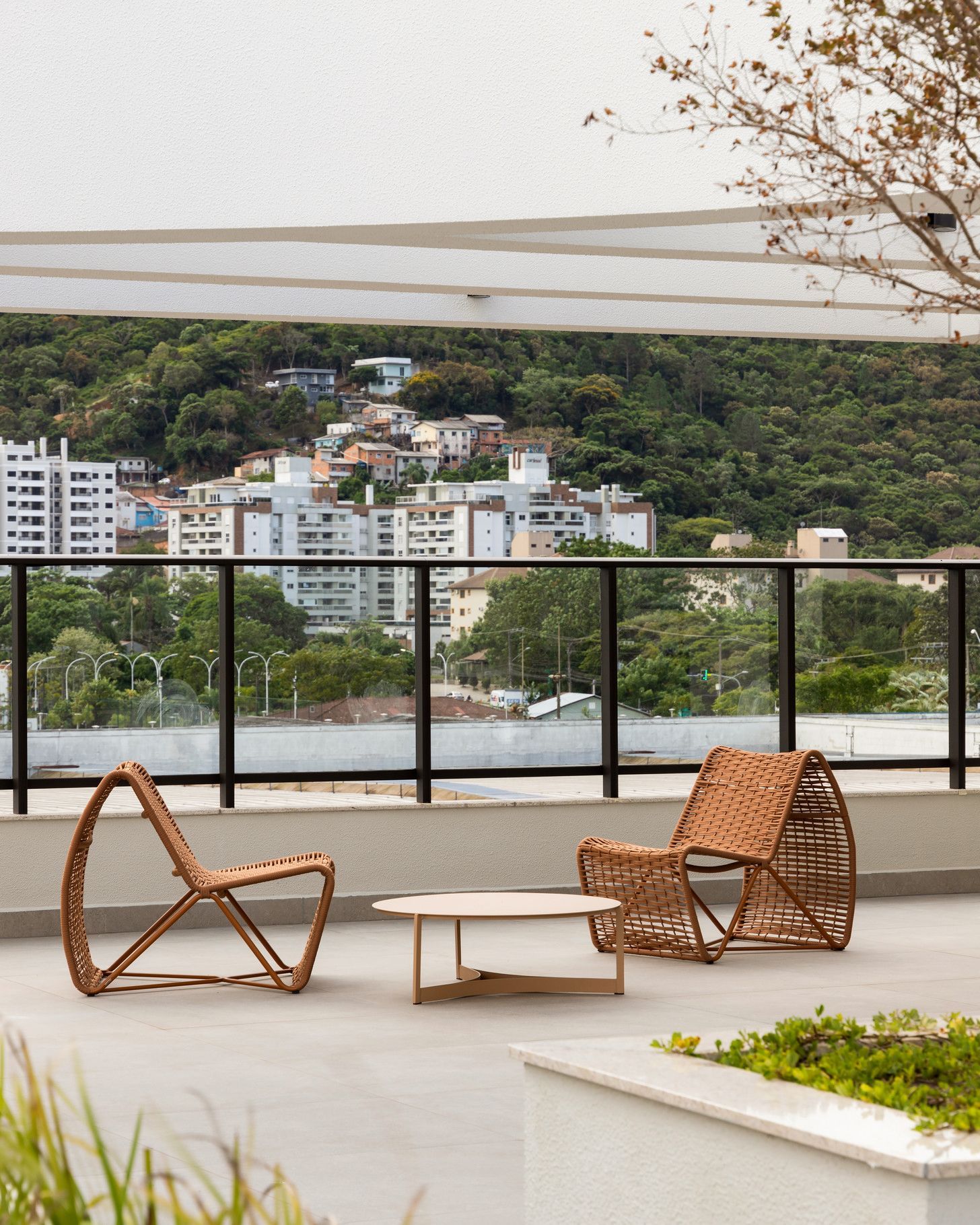 Duas cadeiras de vime e uma mesa em um pátio com vista para a cidade e colinas verdes.