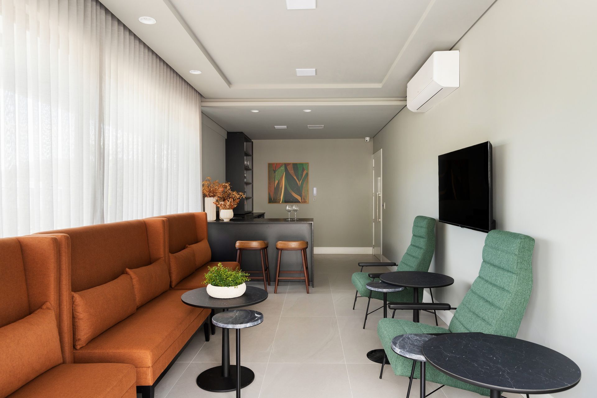 Uma sala de espera moderna com um sofá laranja, cadeiras verdes e um pequeno bar.