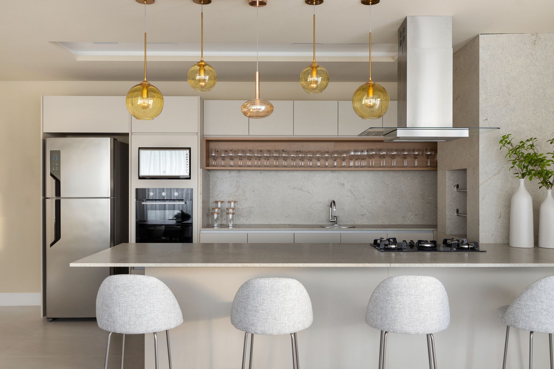 Cozinha moderna com armários de madeira clara, eletrodomésticos de aço inoxidável e luminárias pendentes esféricas.