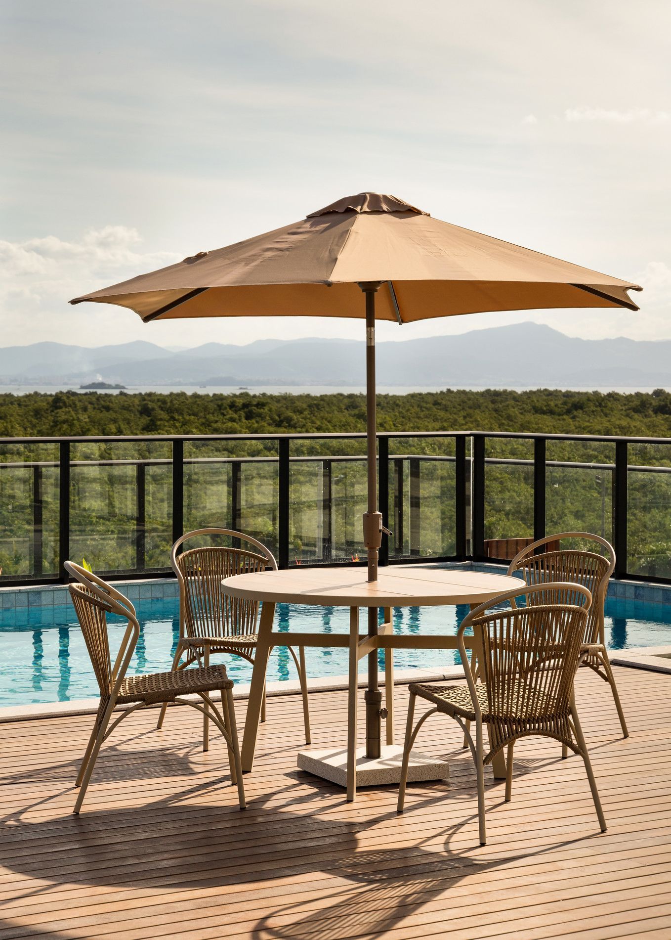 Área de estar ao ar livre com mesa, cadeiras e guarda-sol perto de uma piscina com vista panorâmica.