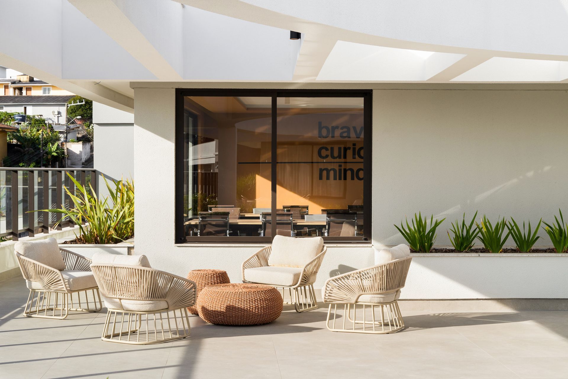 Pátio com cadeiras de vime e uma pequena mesa em frente a uma janela com o texto 