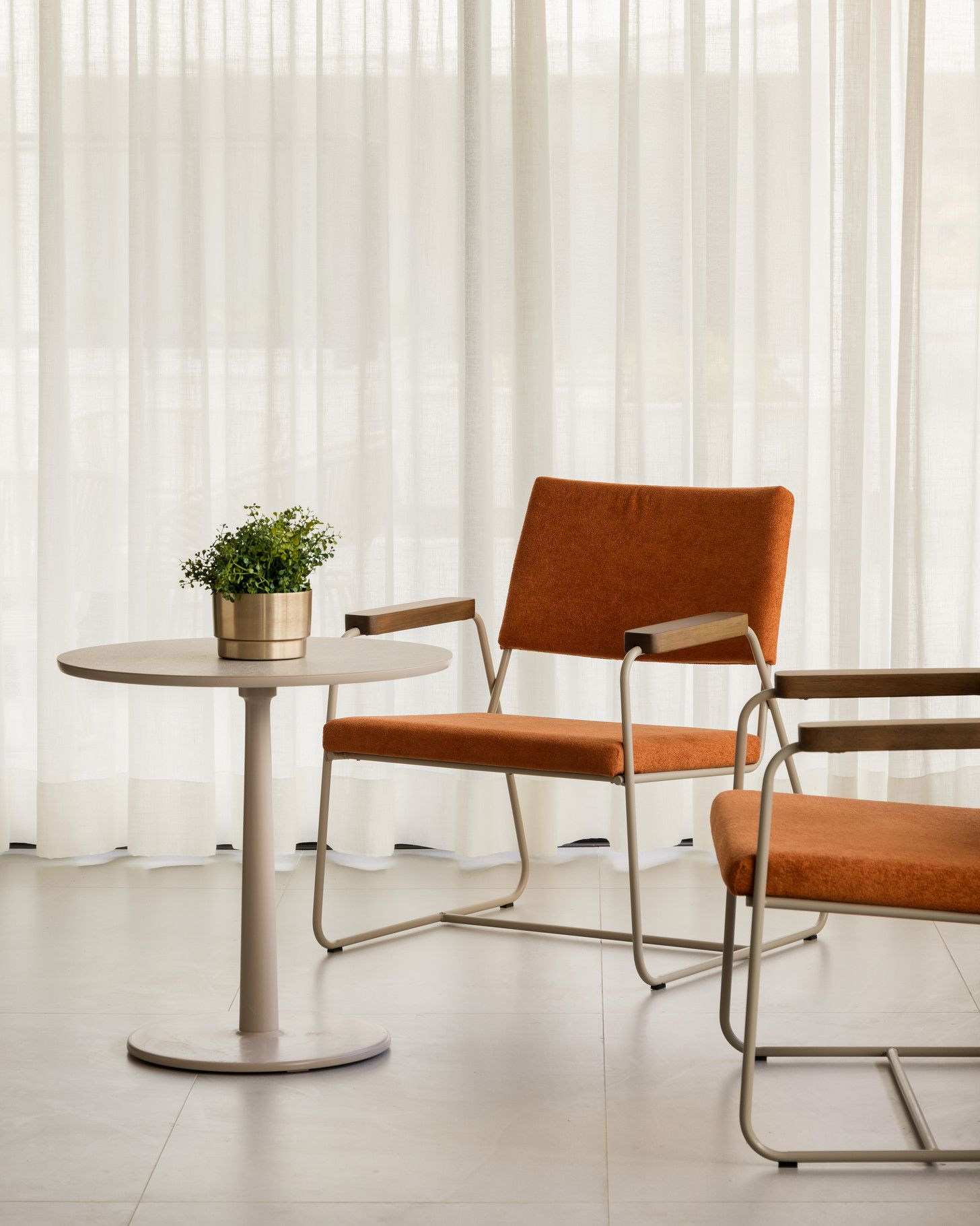 Duas cadeiras modernas laranja de meados do século e uma mesa com plantas em contraste com cortinas brancas.