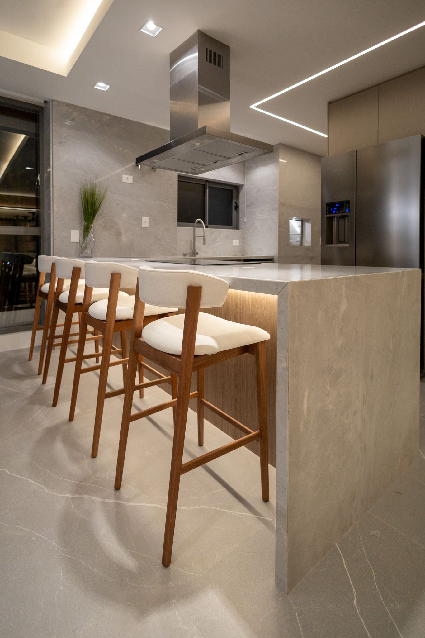 Cozinha com ilha e banquetas de madeira. Coifa de aço inoxidável sobre a bancada.