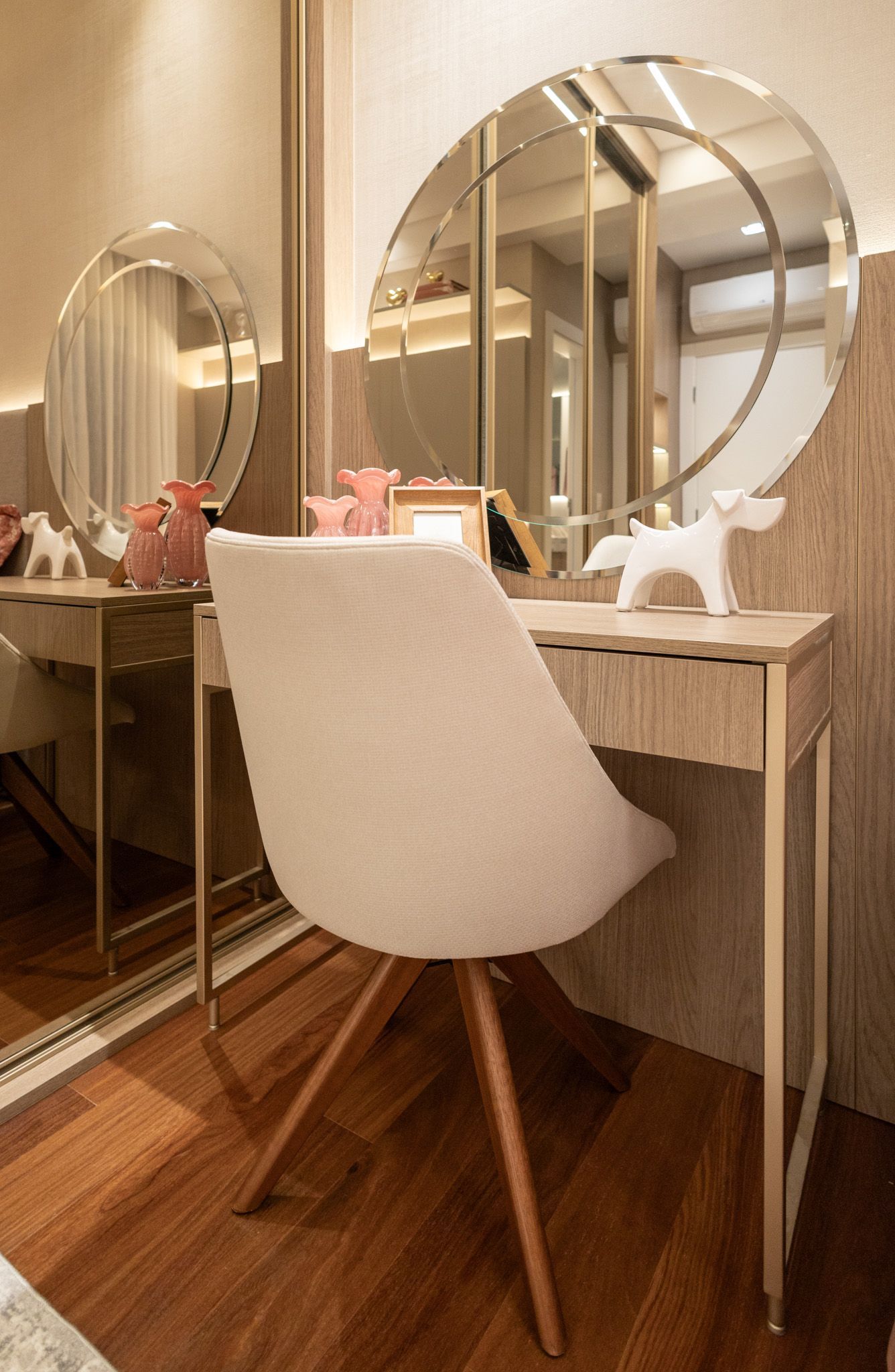 Toucador com espelhos redondos, cadeira branca, detalhes em madeira e dourado.