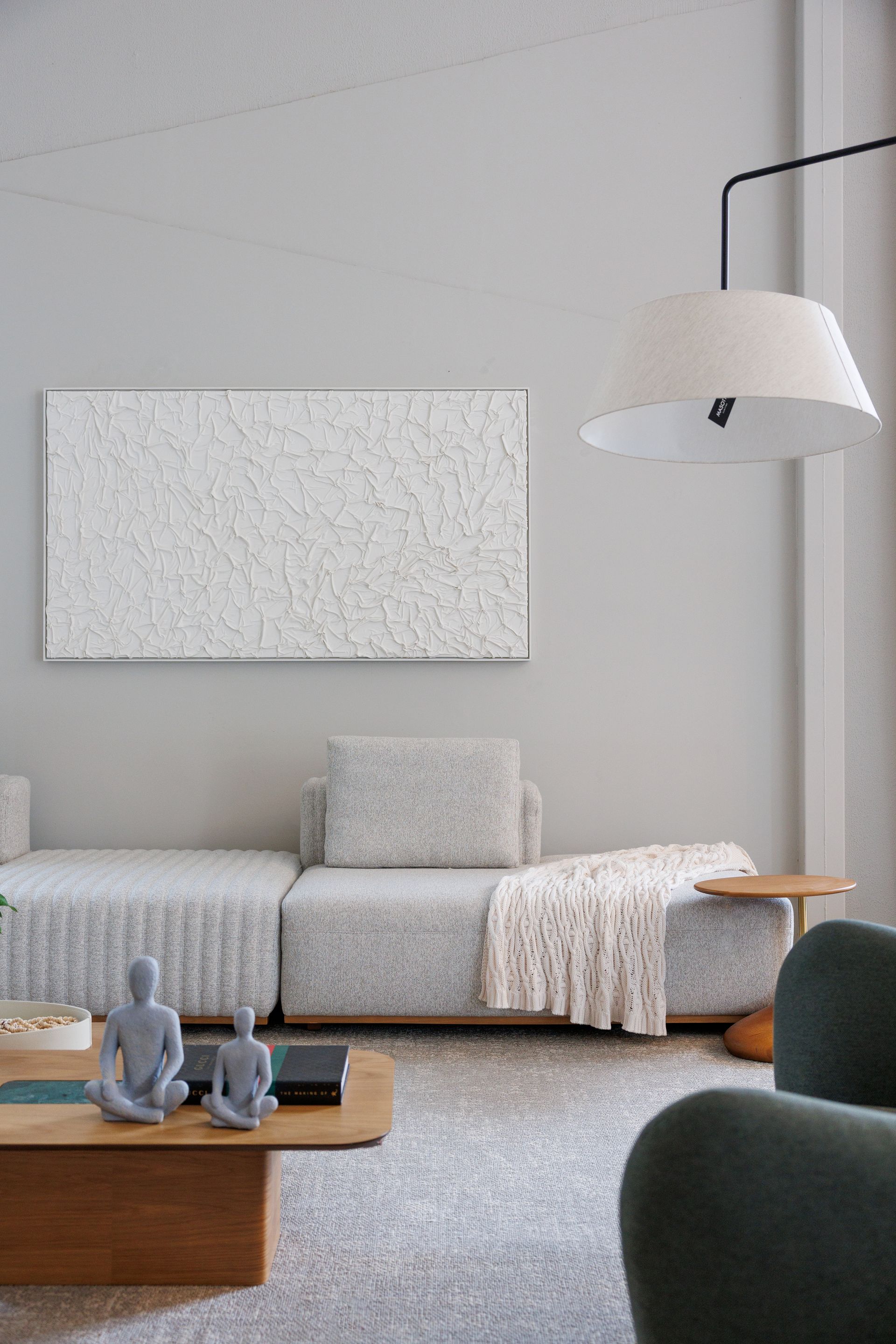 Sala de estar com sofá cinza, arte abstrata, luminária de chão, mesa de centro de madeira e poltrona azul-petróleo.