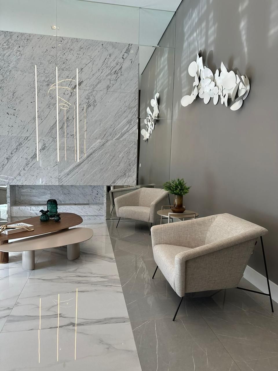 Hall de entrada moderno com parede de mármore, cadeiras e arte abstrata.