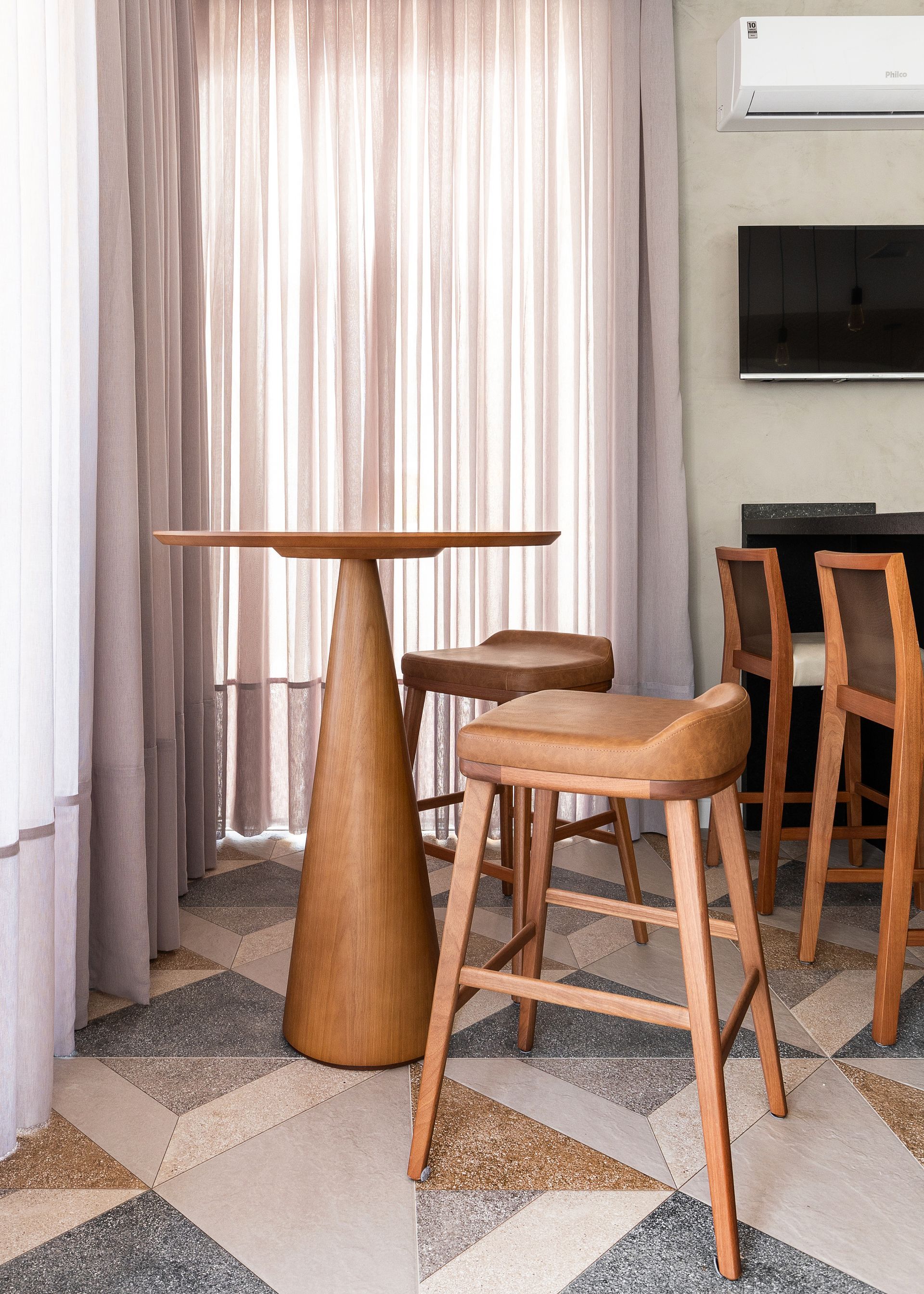 Uma sala com mesa alta, bancos, bar, televisão e piso frio. Tons neutros por toda parte.