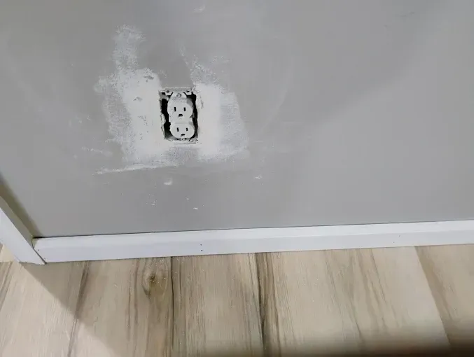 A electrical outlet is being installed on a wall next to a wooden floor.
