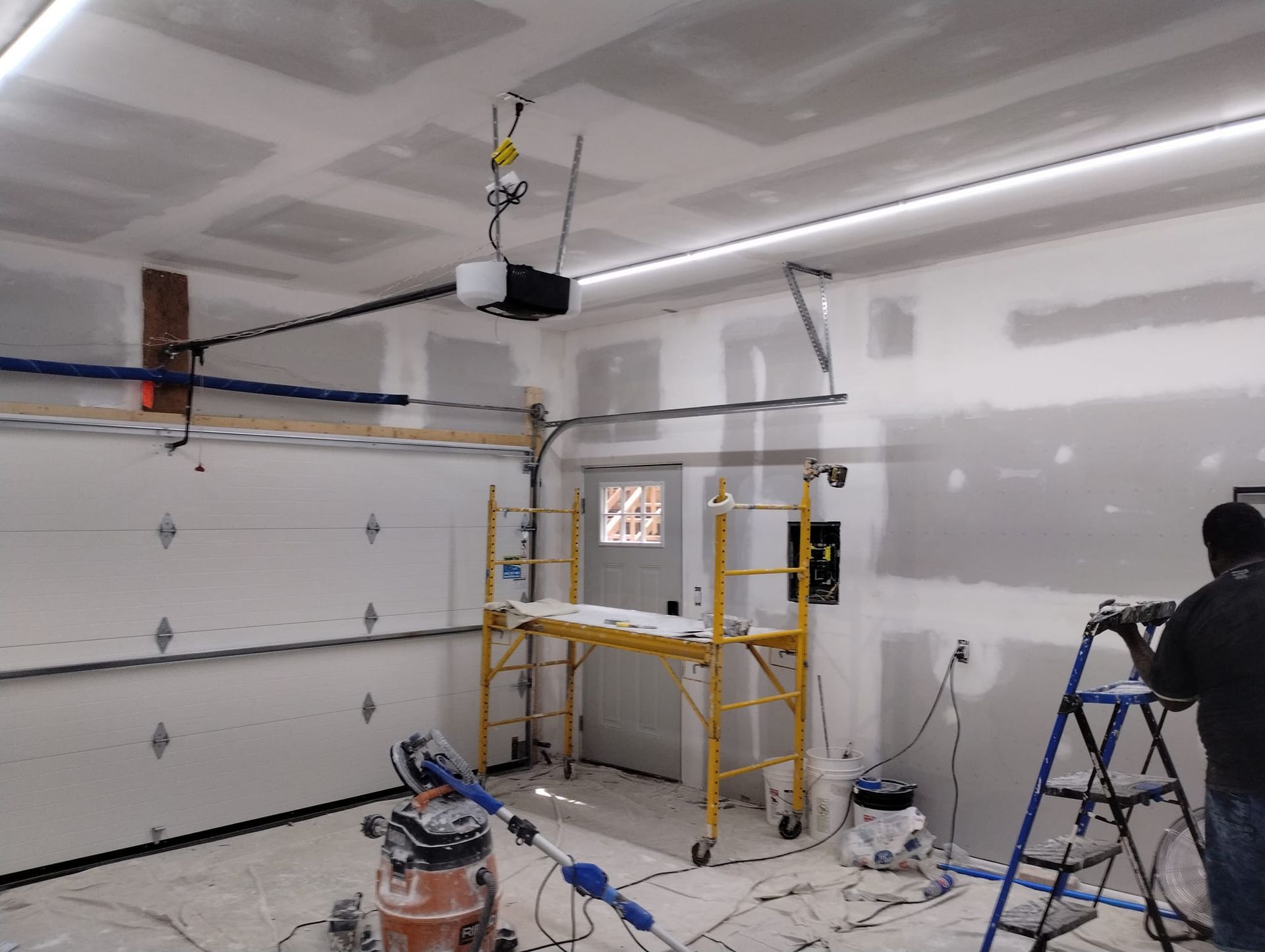 A man is painting a garage door with a vacuum cleaner.