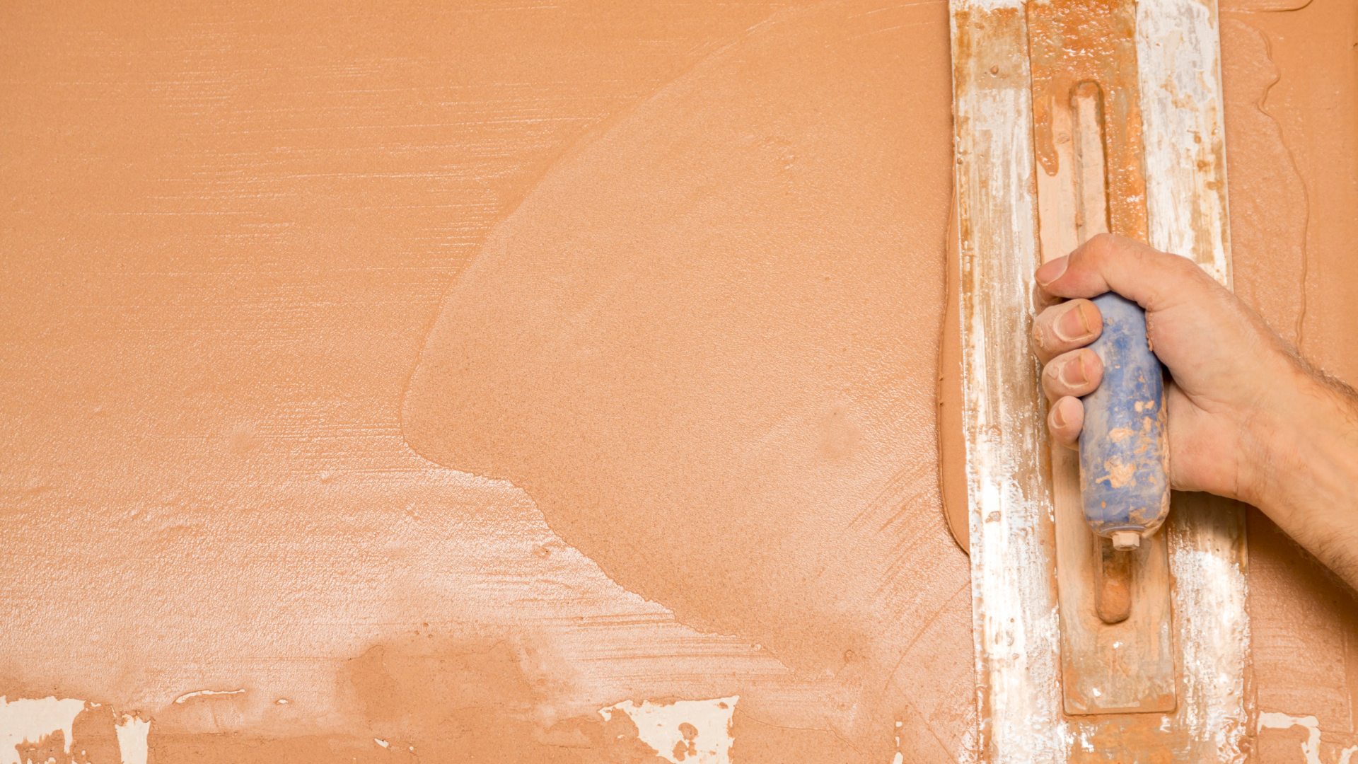 A person is plastering a wall with a trowel.