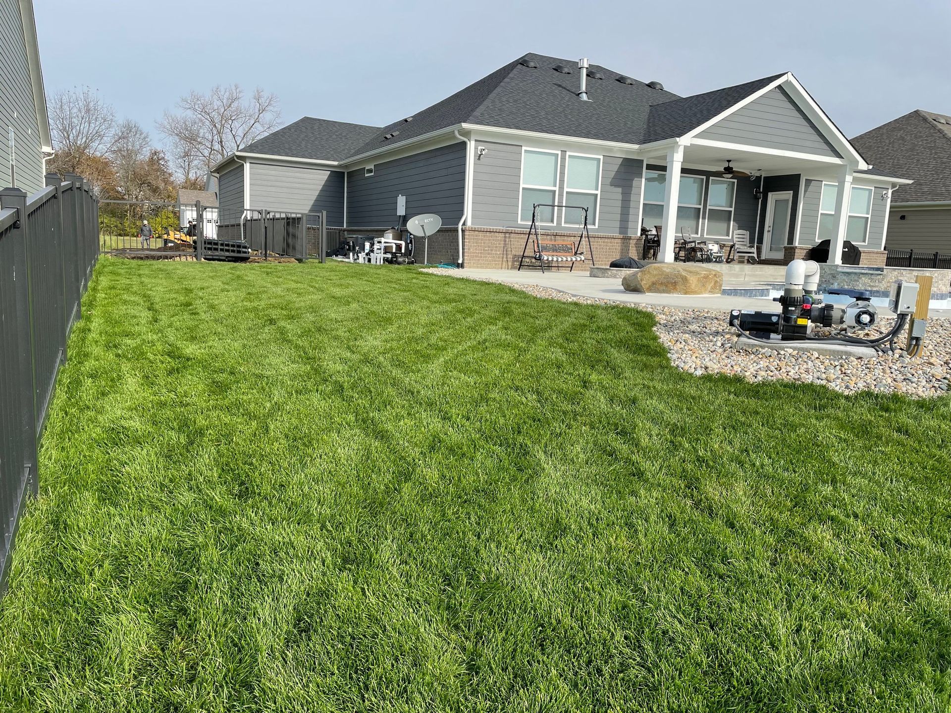 Backyard with green grass, gray house, and patio.