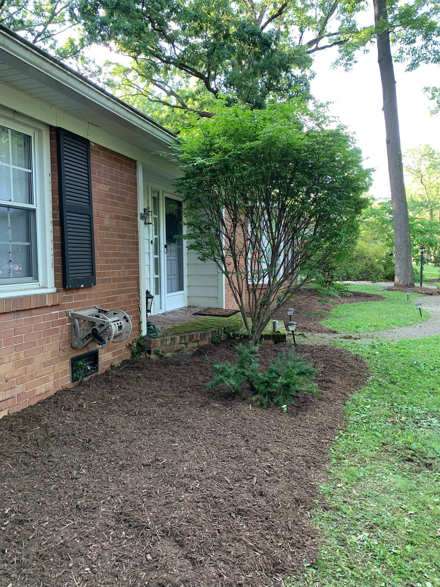 Brick house with black shutters, mulch flower bed, and green shrubbery.