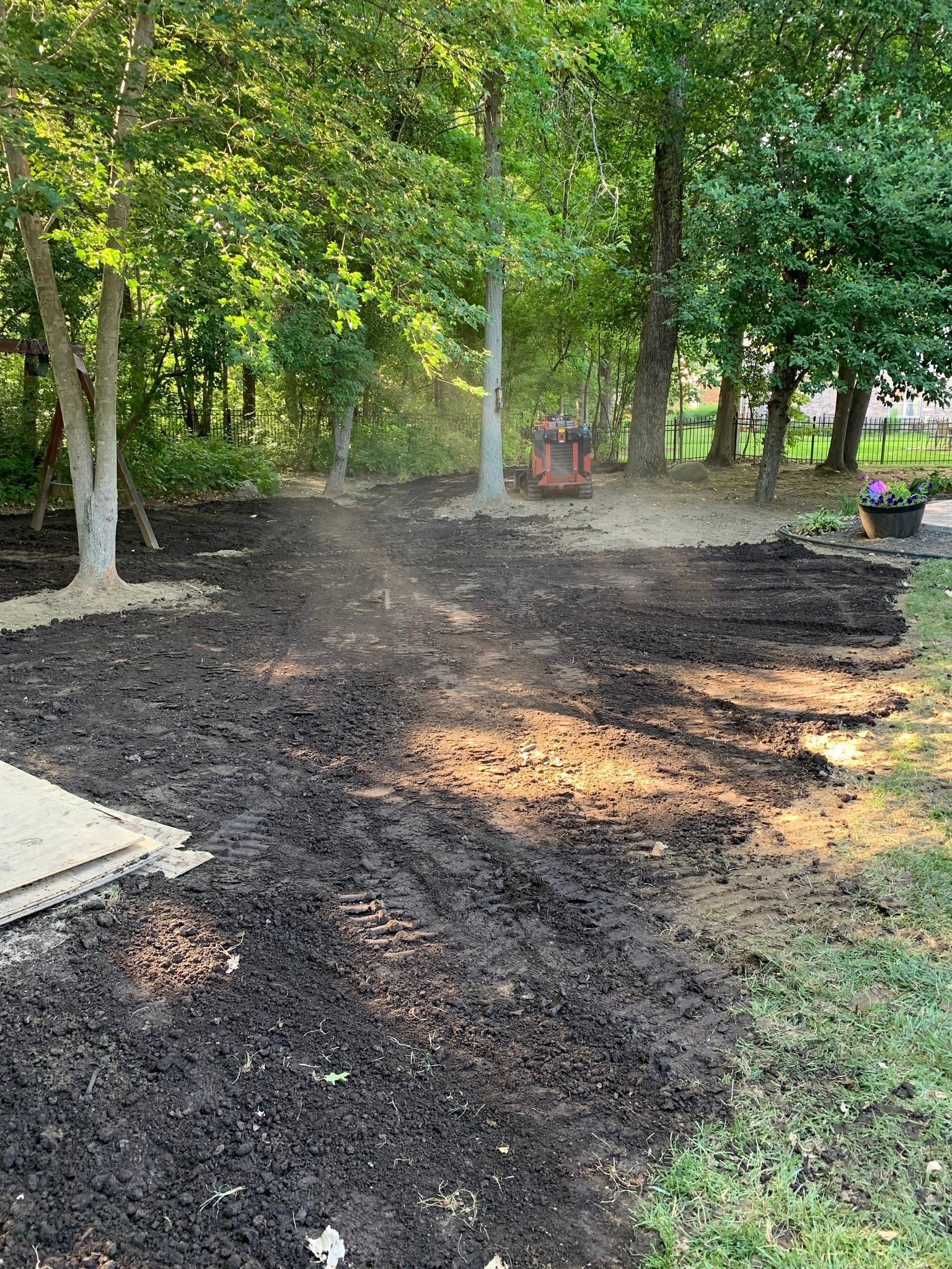 Freshly tilled dark soil in a backyard, surrounded by trees and greenery.
