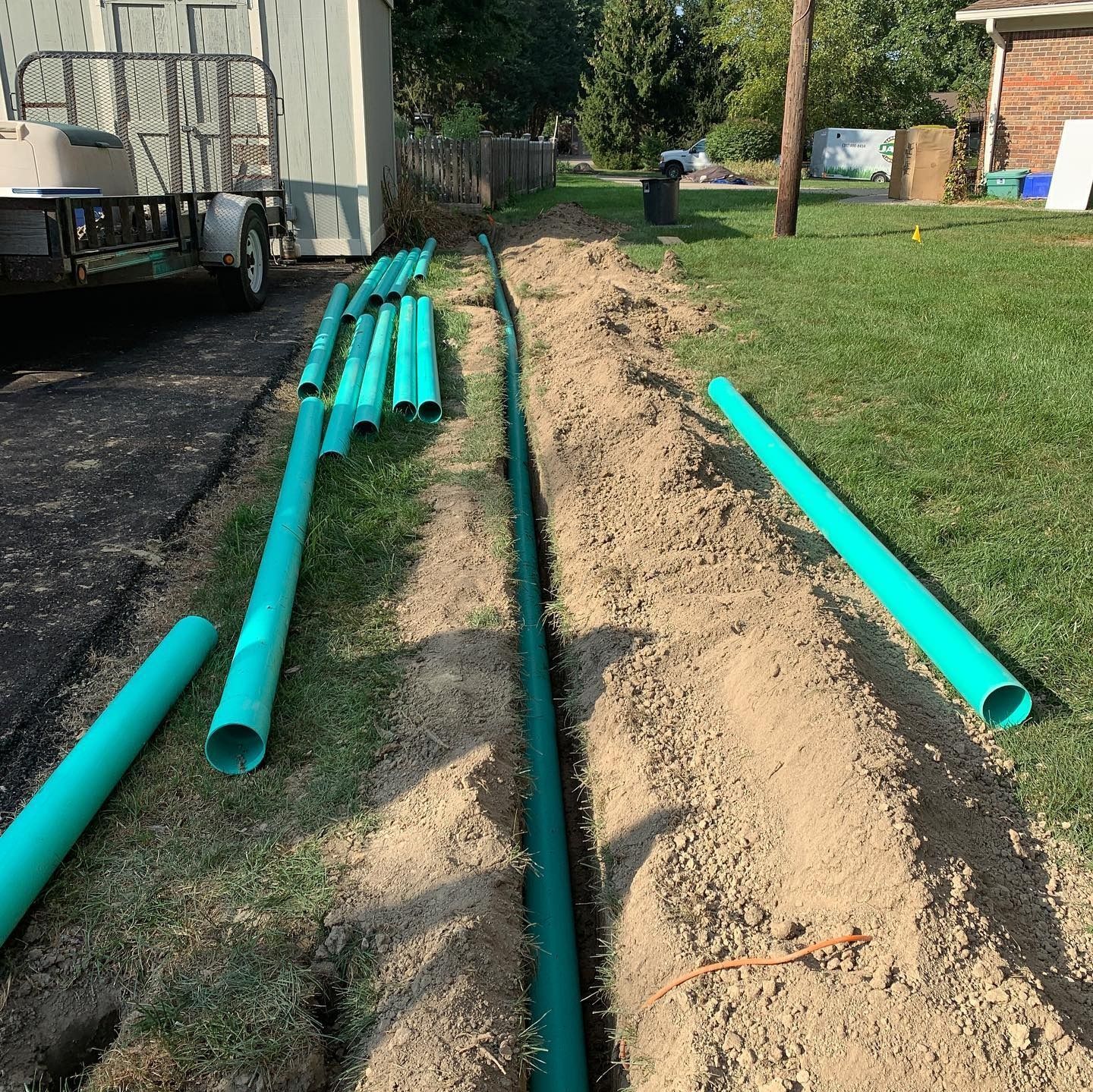 A trench dug in the grass with green pipes for drainage.