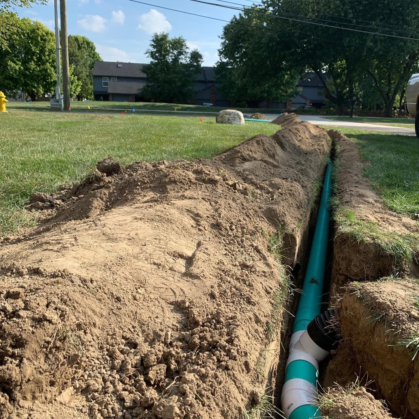 A trench with a green and white pipe installed in the ground, on a grassy lawn.