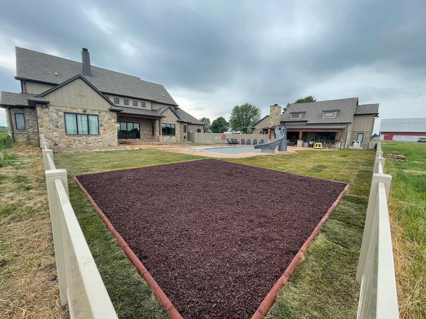 Large house with a backyard featuring a gravel area bordered by a white fence and lush green grass.
