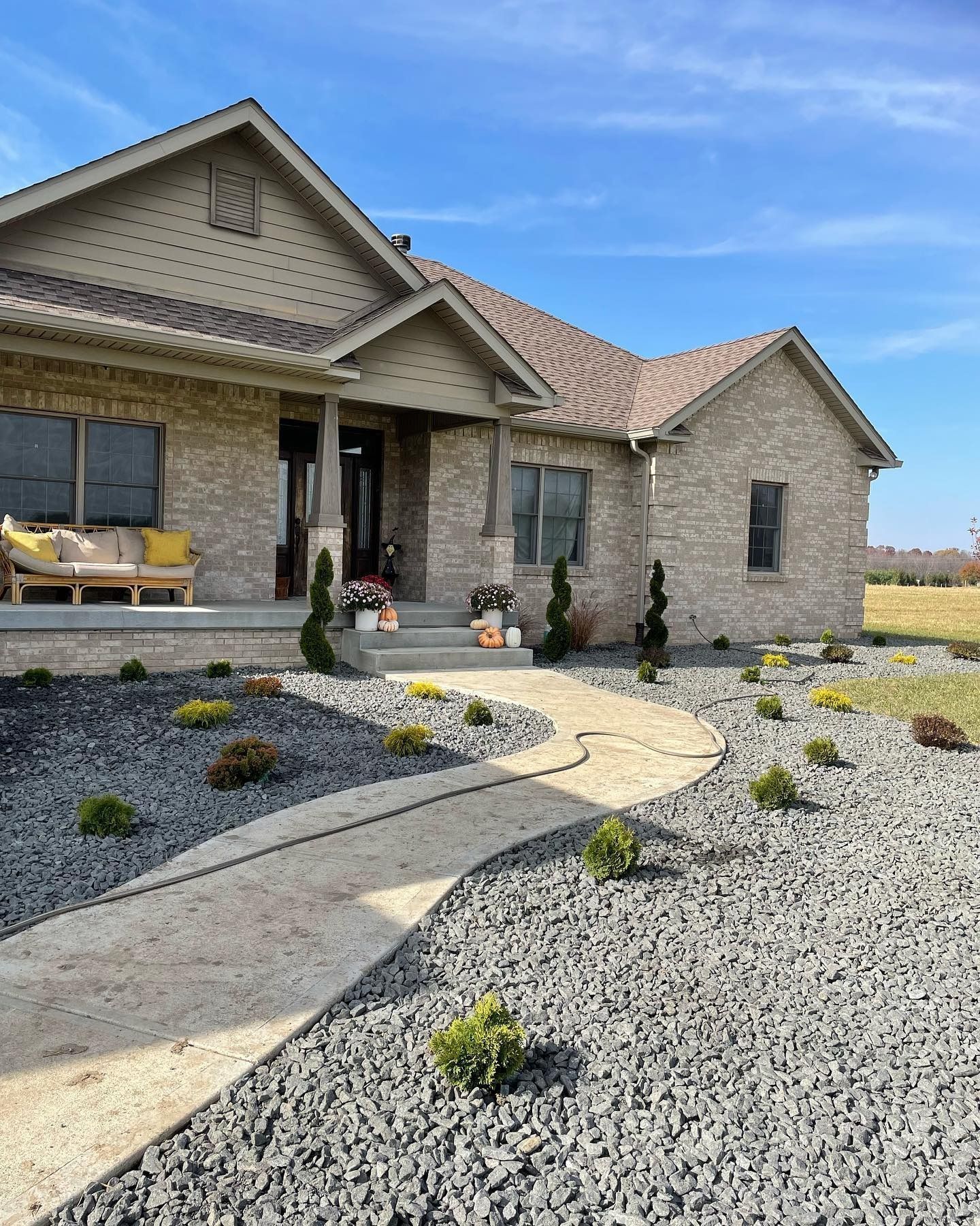 Stone home with a curved walkway, featuring landscaping and a blue sky.