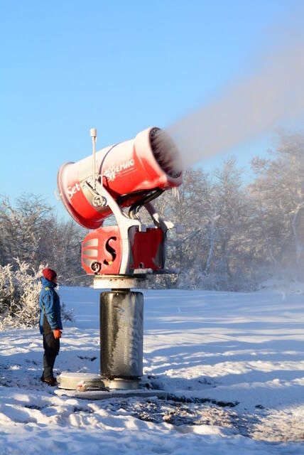 Un hombre está parado frente a un cañón de nieve con la letra s en él.