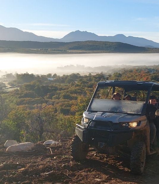 Un vehículo todo terreno está estacionado en la cima de una colina con montañas al fondo.