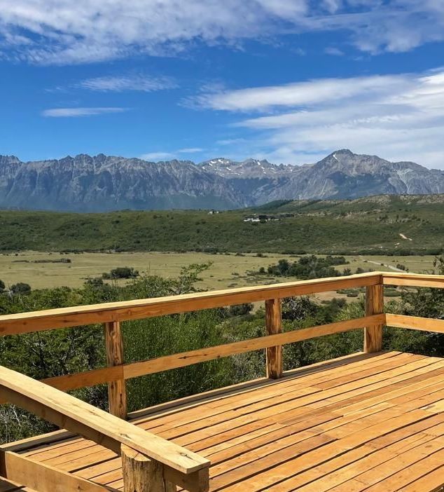 Una terraza de madera con vistas a un valle con montañas al fondo.
