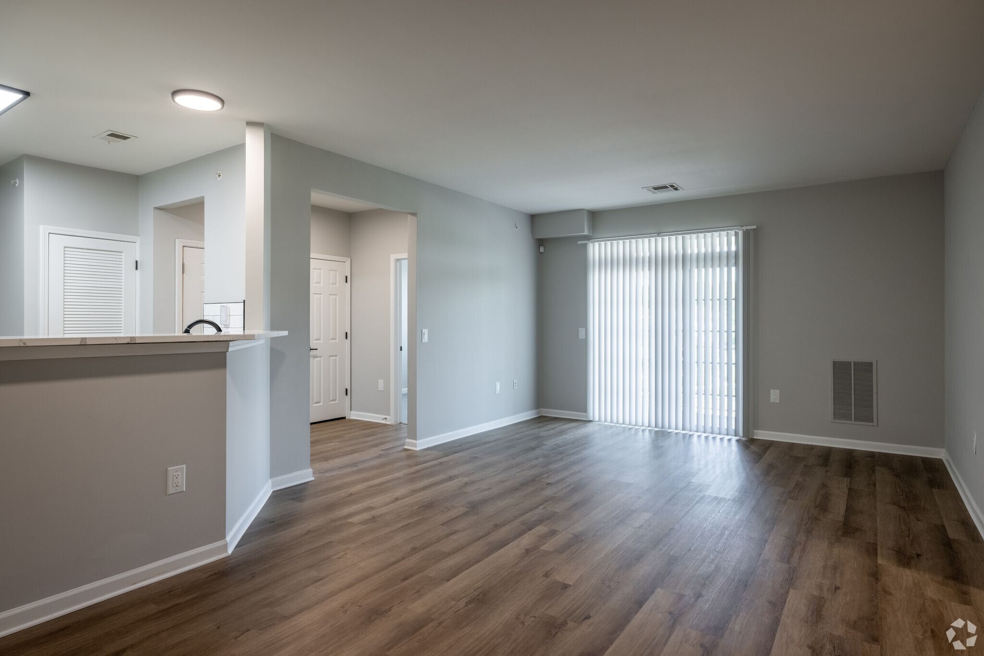 Open living area with a breakfast bar and sliding door with vertical blinds.