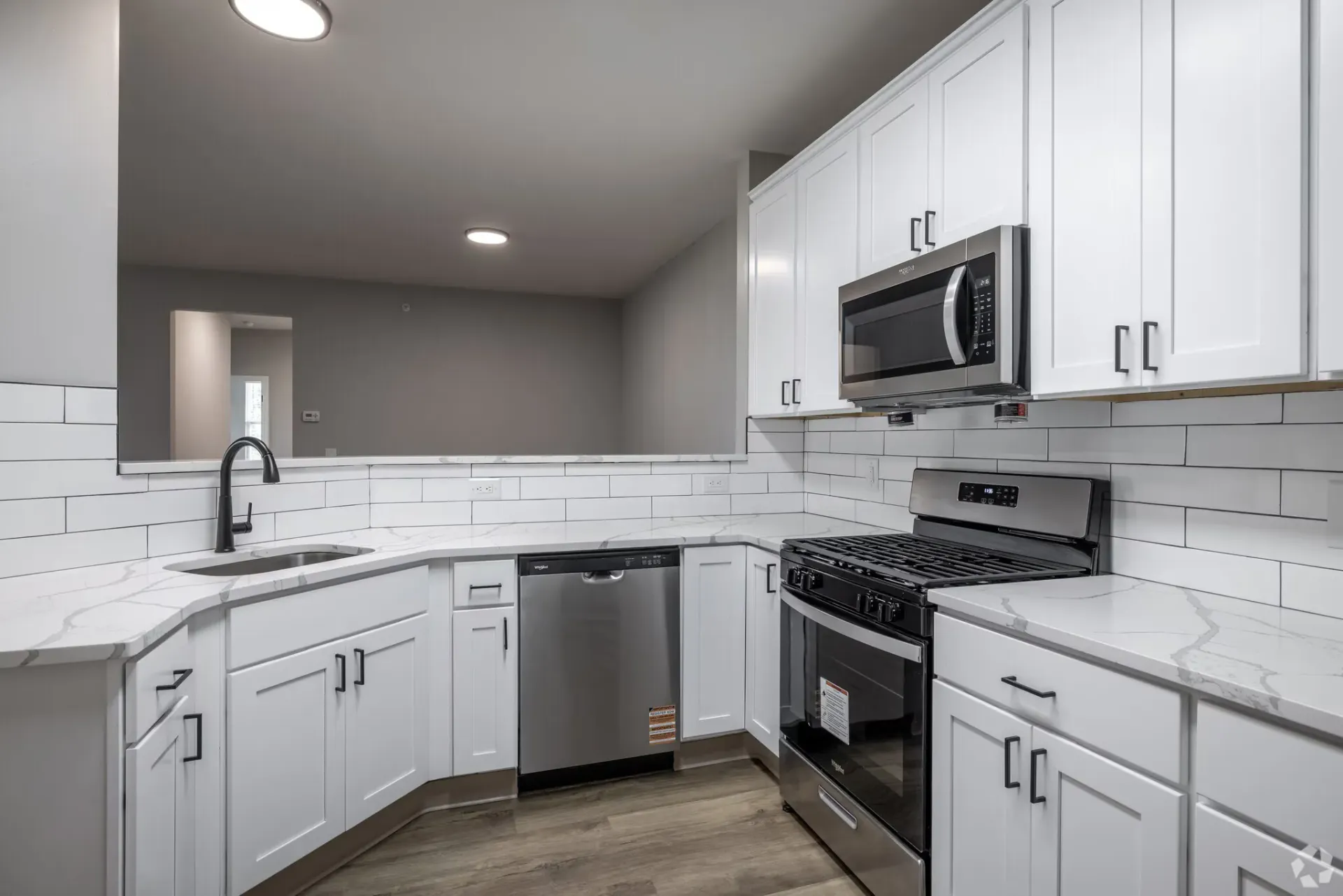 White kitchen with marble-pattern countertops, subway tile backsplash, and stainless steel appliances.