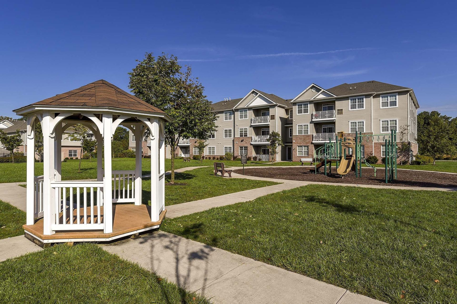 White gazebo in a green apartment courtyard with a playground and multi-story buildings.