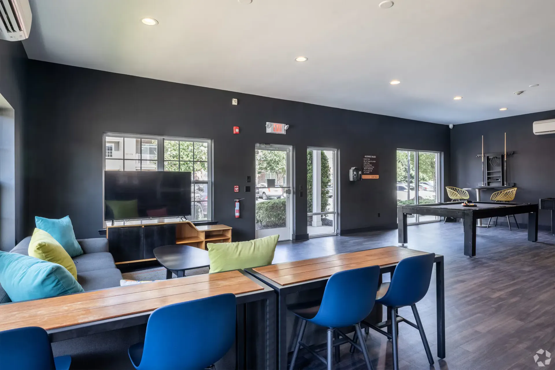 Interior community lounge with dark walls, windows, TV, and seating.