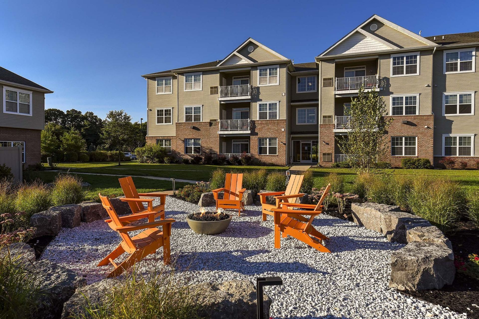 Outdoor community courtyard with a fire pit and orange chairs in front of apartment buildings