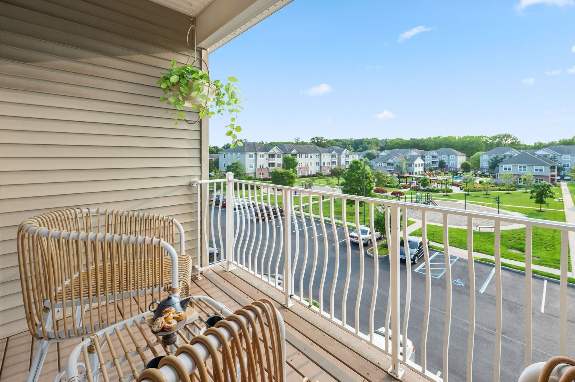 Private balcony with wicker chairs and hanging plant, overlooking a landscaped apartment community.