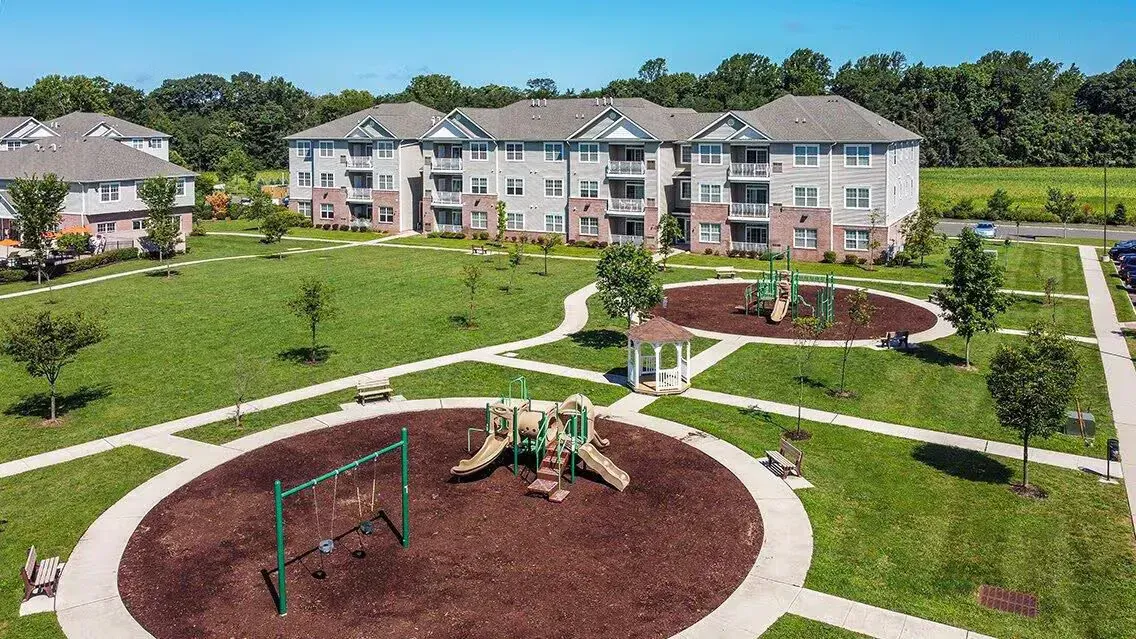 Aerial view of a multi-building apartment community with a playground, gazebo, and green lawns.