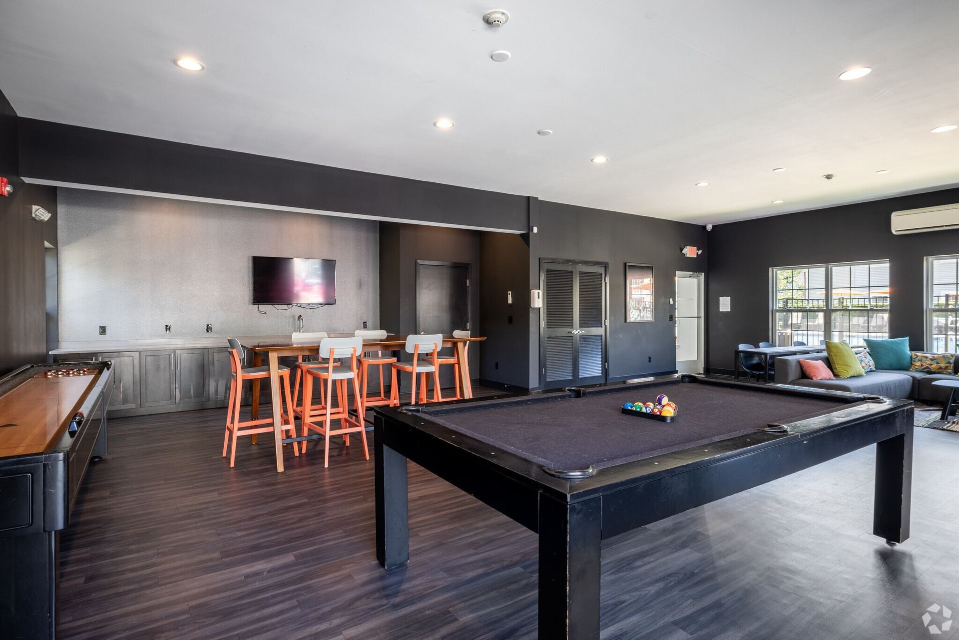 Indoor resident lounge with a pool table, bar-height tables, and a wall-mounted TV.