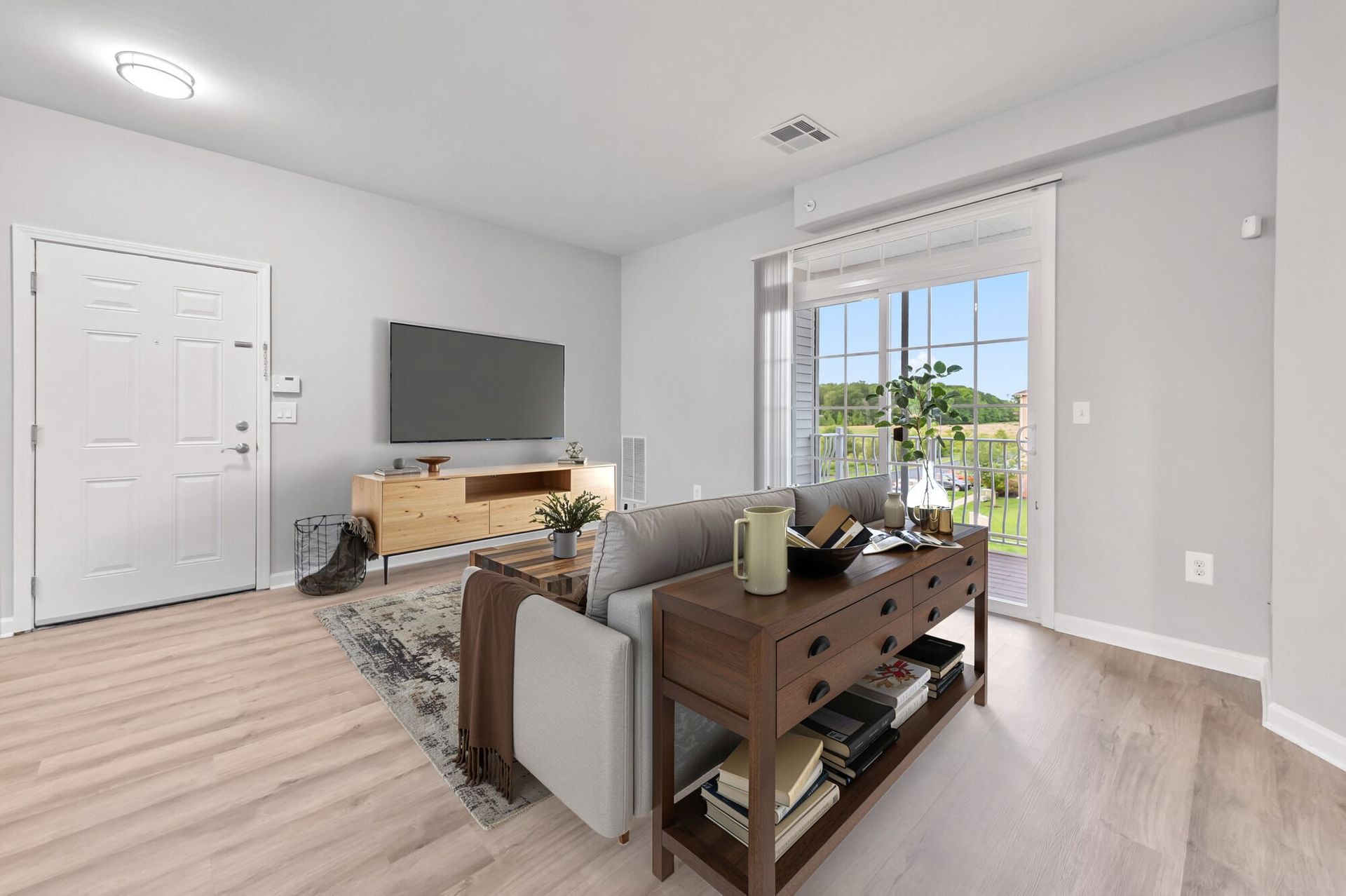 Living room in an apartment with a sofa, TV on a wooden credenza, and a glass sliding door to a balcony.