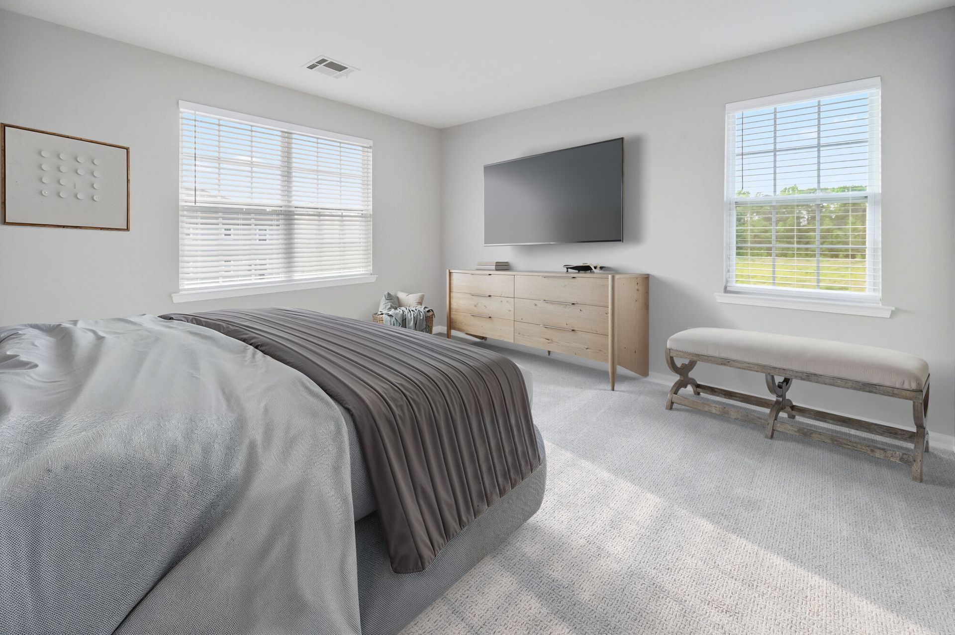 Bright apartment bedroom with a large bed, wooden dresser with TV, and a bench by the window.