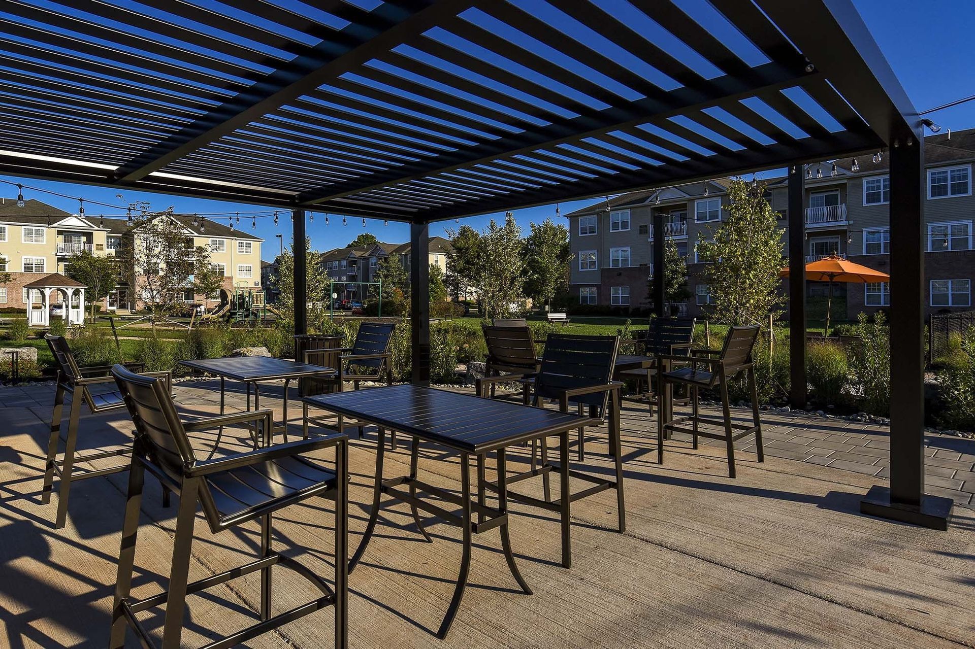 Outdoor communal patio with black metal tables and chairs under a slatted pergola.