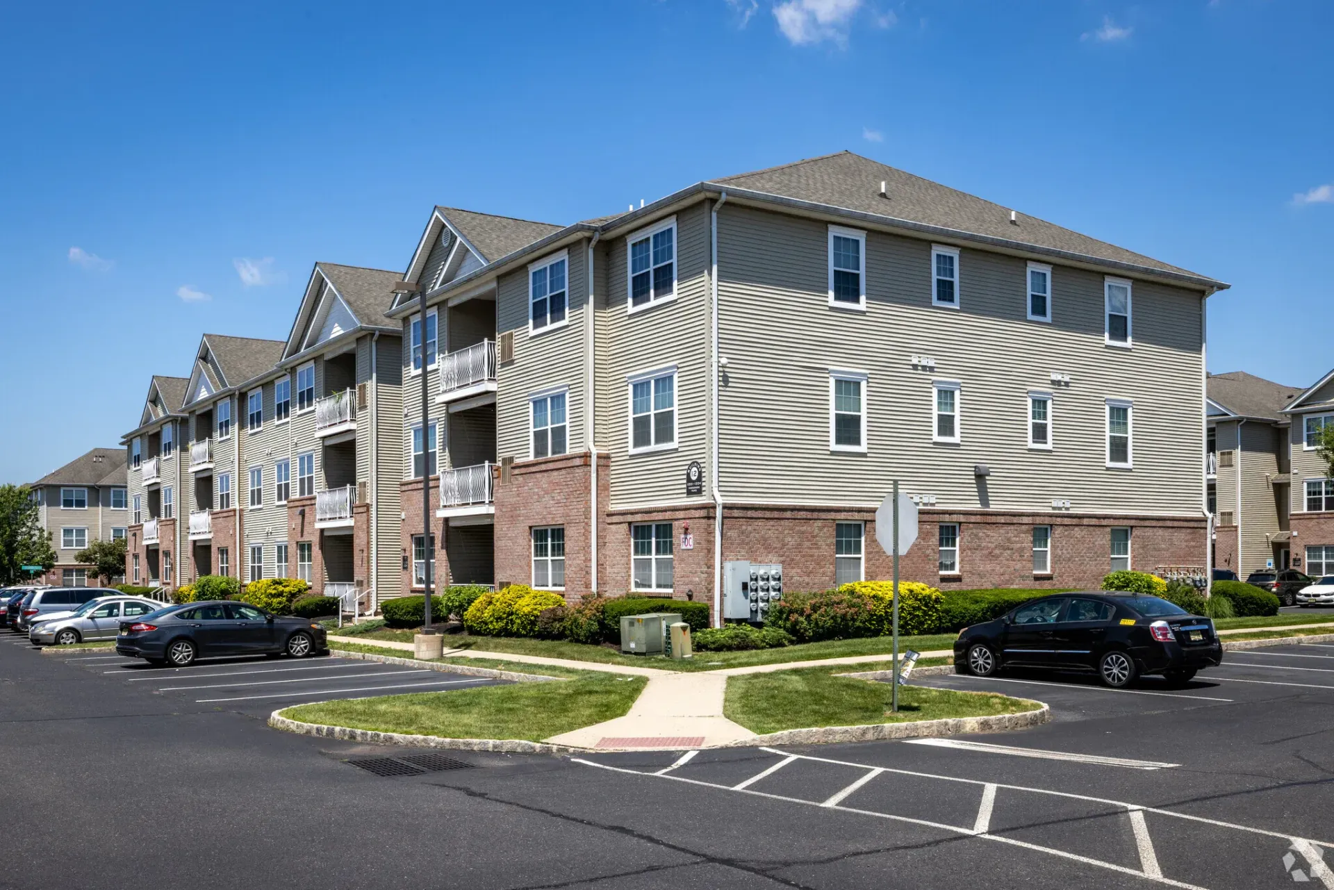 Exterior view of a multi-story apartment building with brick base, beige siding, and a surrounding parking lot.