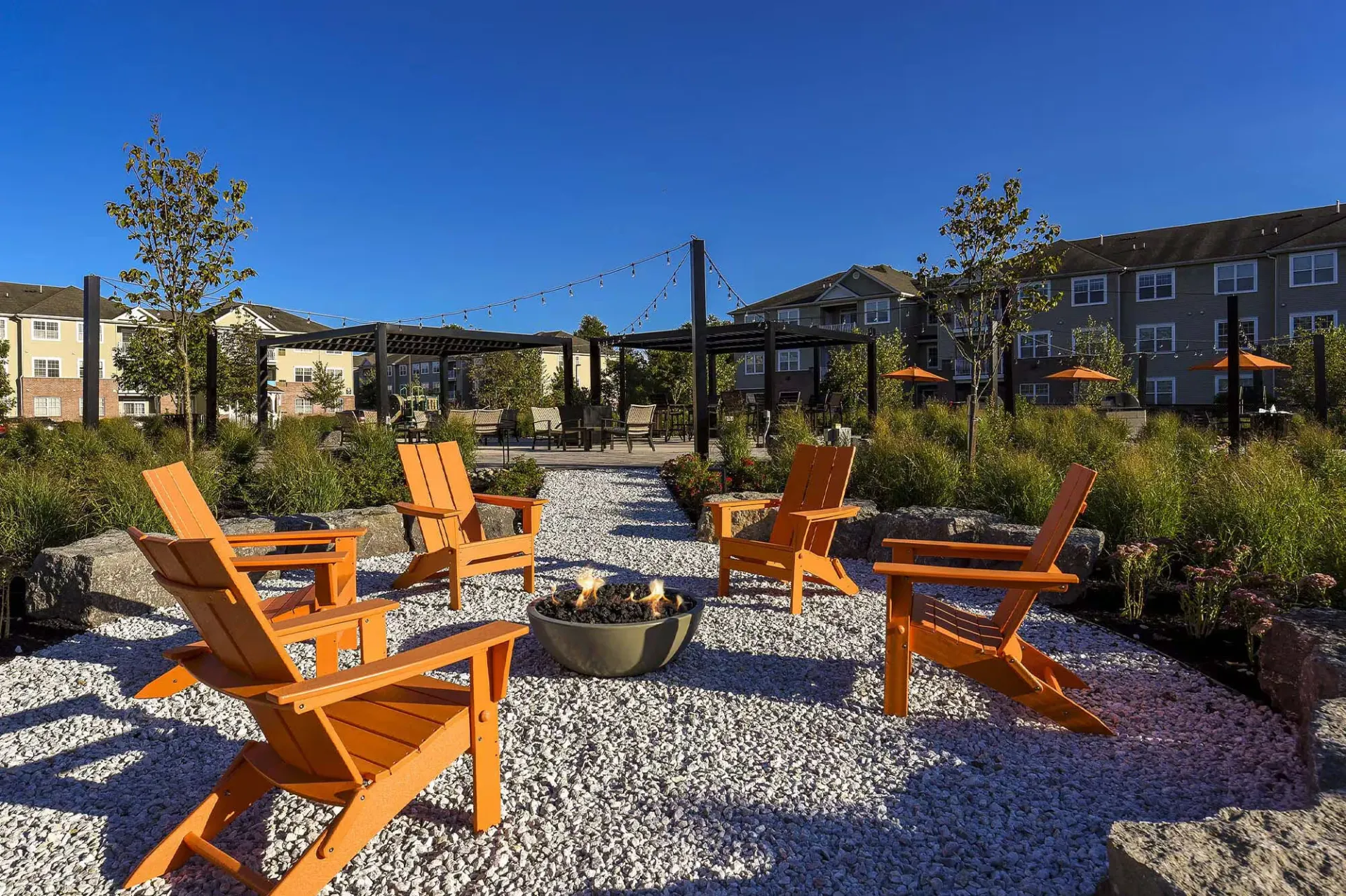 Outdoor community courtyard with orange Adirondack chairs around a fire pit and string lights.