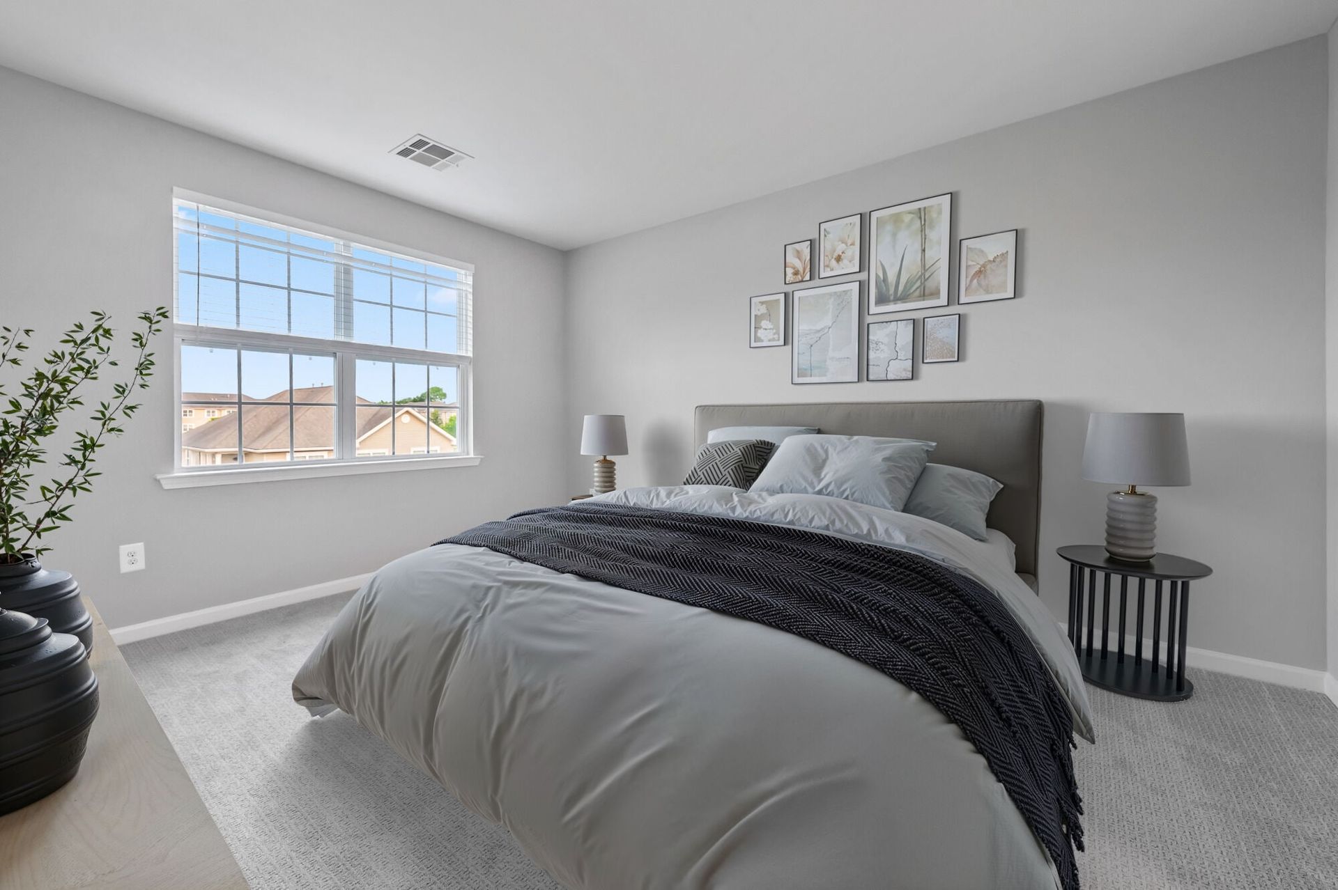 Bedroom in an apartment with a neatly made bed, two nightstands, lamps, and wall art.