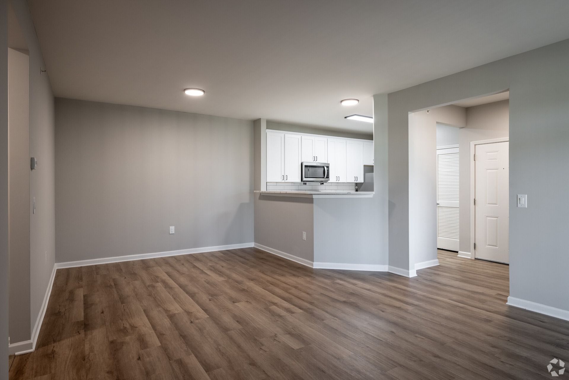 Open living area with laminate wood flooring, white kitchen cabinets, and a pass-through counter.