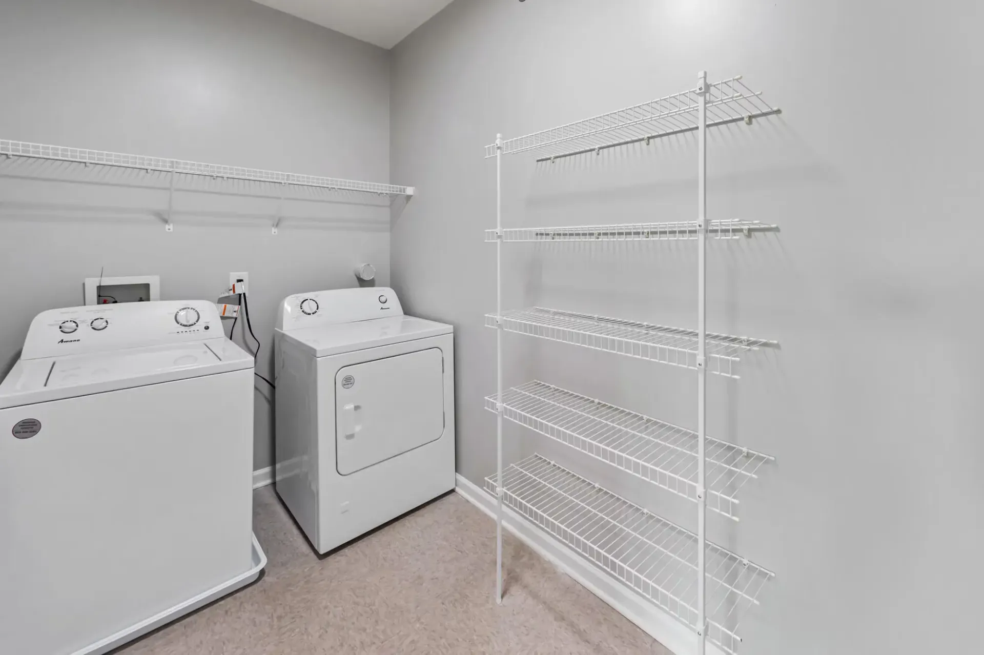 Laundry room with a washer and dryer and white wire shelving along the walls.