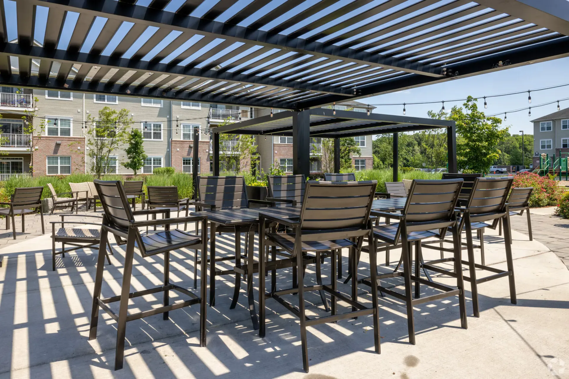 Outdoor community lounge with metal pergolas, string lights, and patio seating.