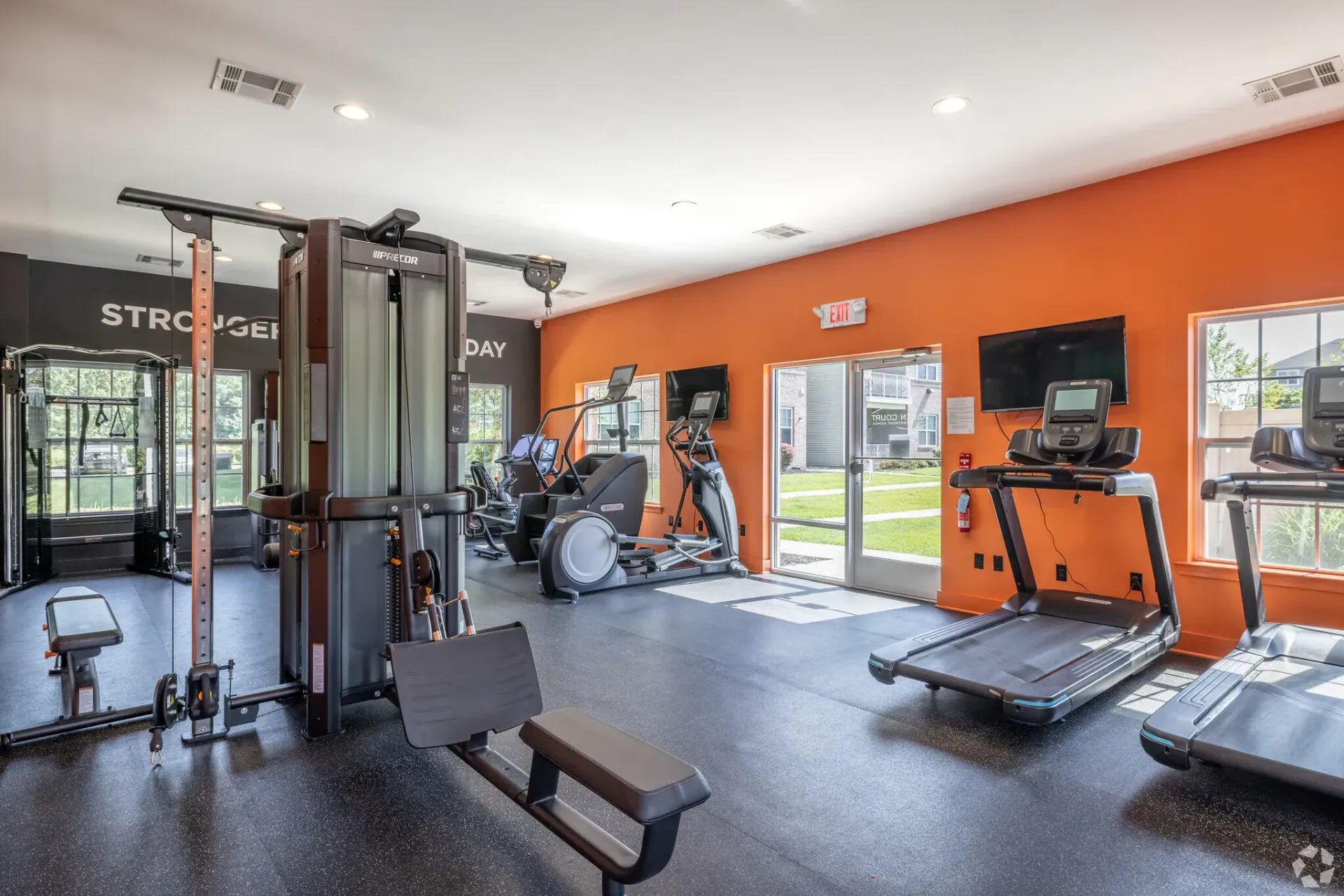 Fitness center with cardio machines, weight station, and bright orange wall.
