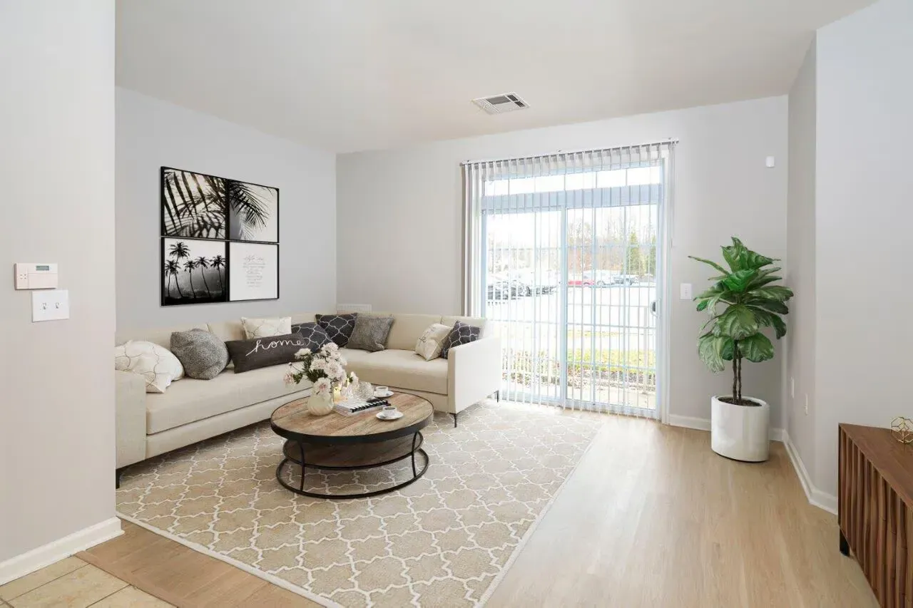 Bright living room with a beige sectional, round coffee table, and sliding glass door to a balcony.