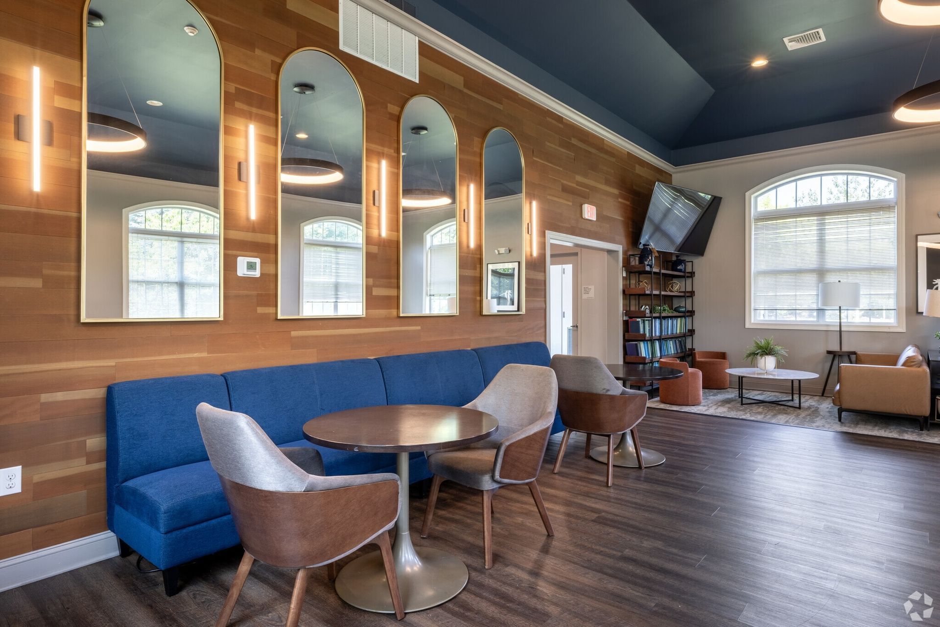 Interior resident lounge with blue seating, round tables, arched mirrors, and wood-paneled walls.