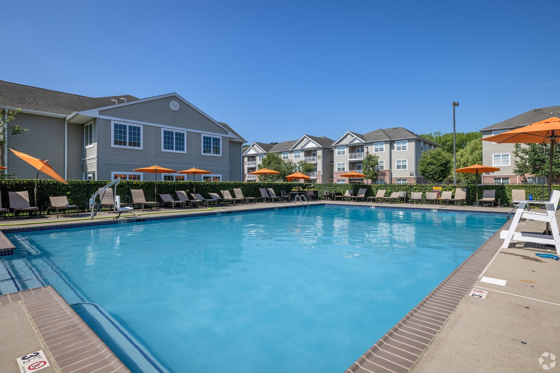 Outdoor pool at a residential community with lounge chairs and orange umbrellas.