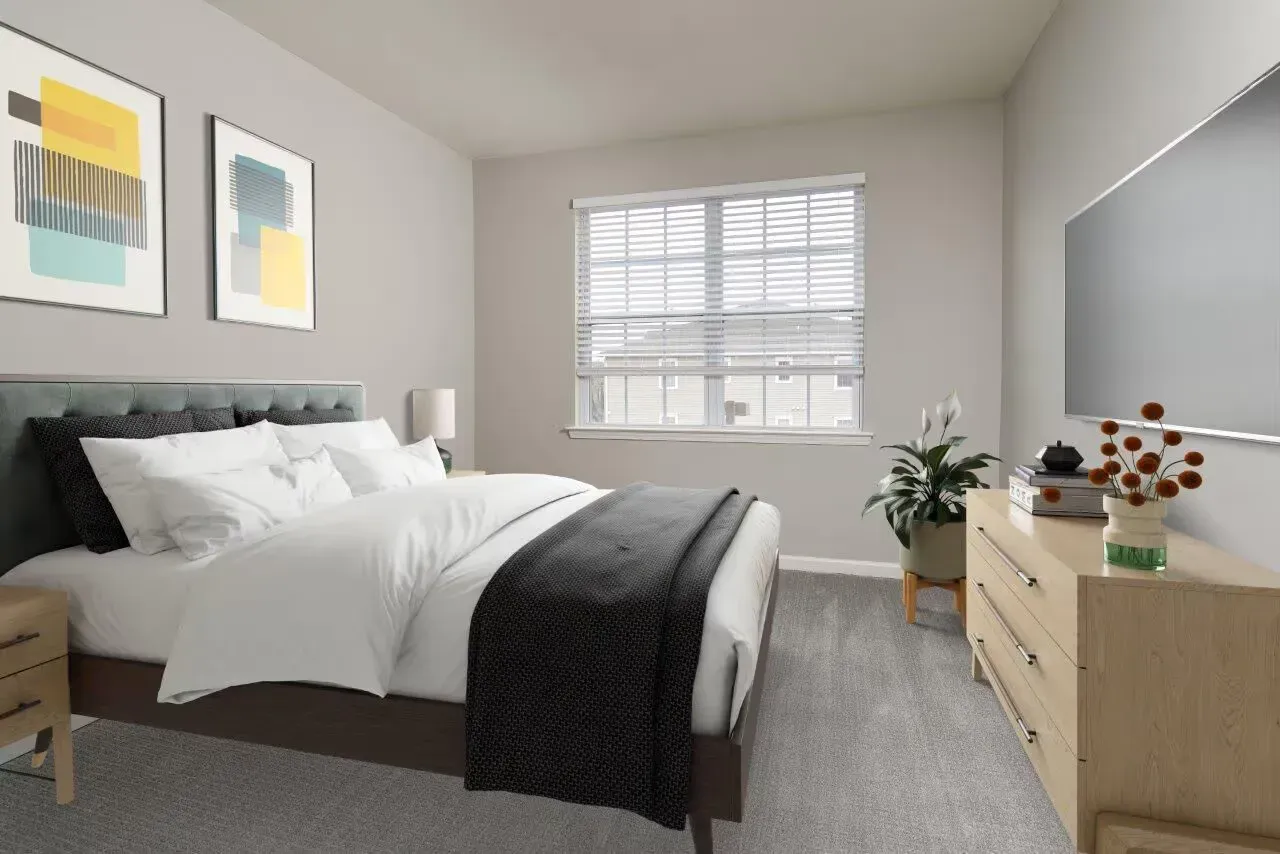 Modern apartment bedroom with a bed, dresser, plant, and a large window.