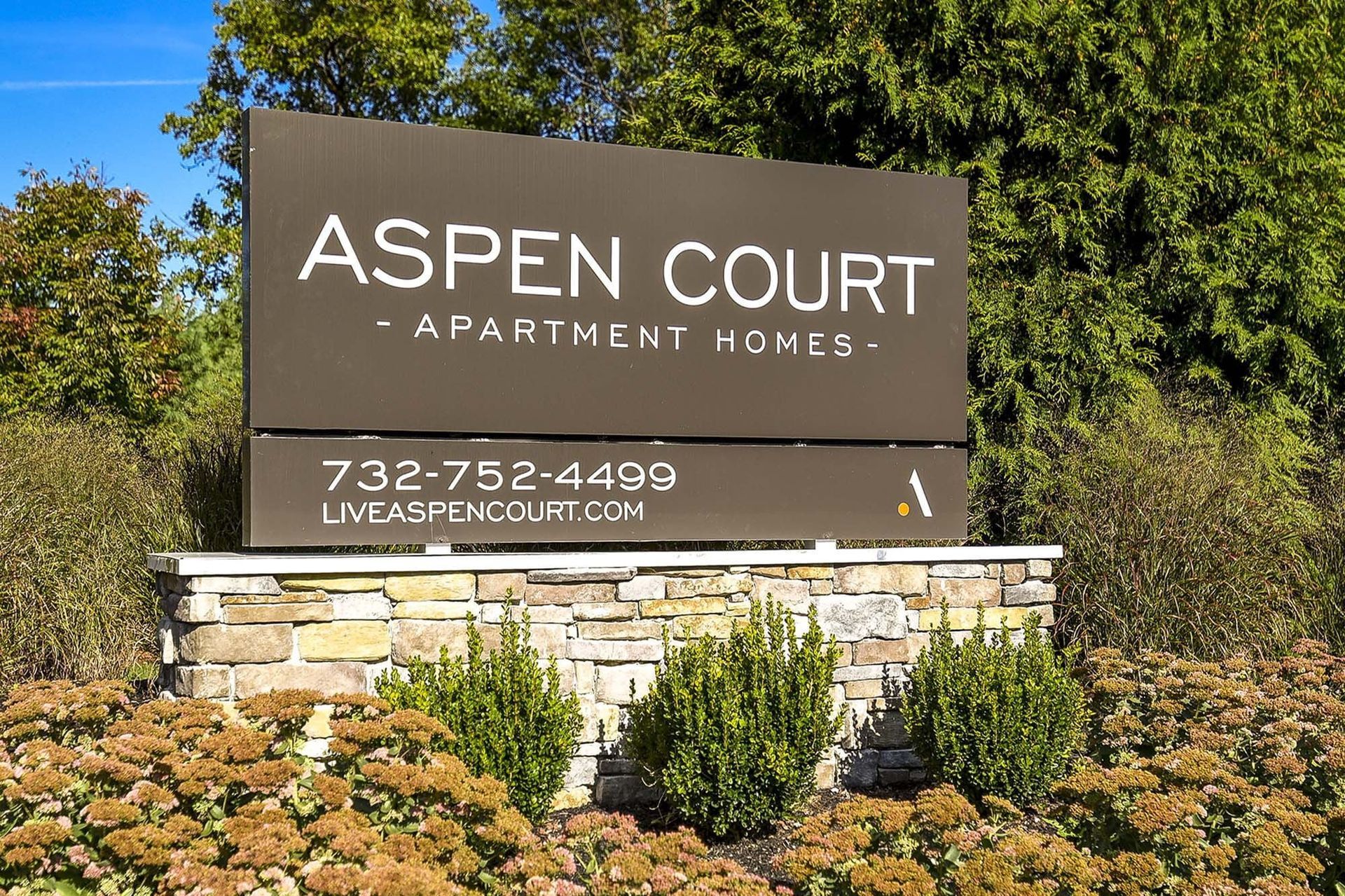 Exterior sign for Aspen Court Apartment Homes with a stone base and landscape.