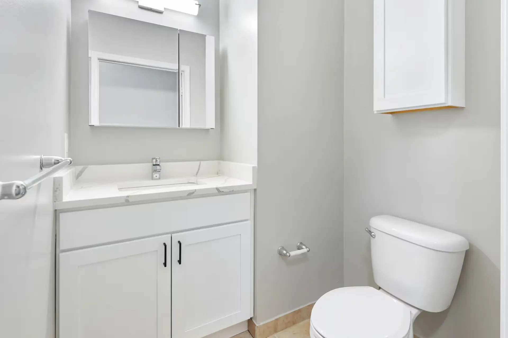 Bright apartment bathroom with a white vanity, sink, mirror, and toilet.