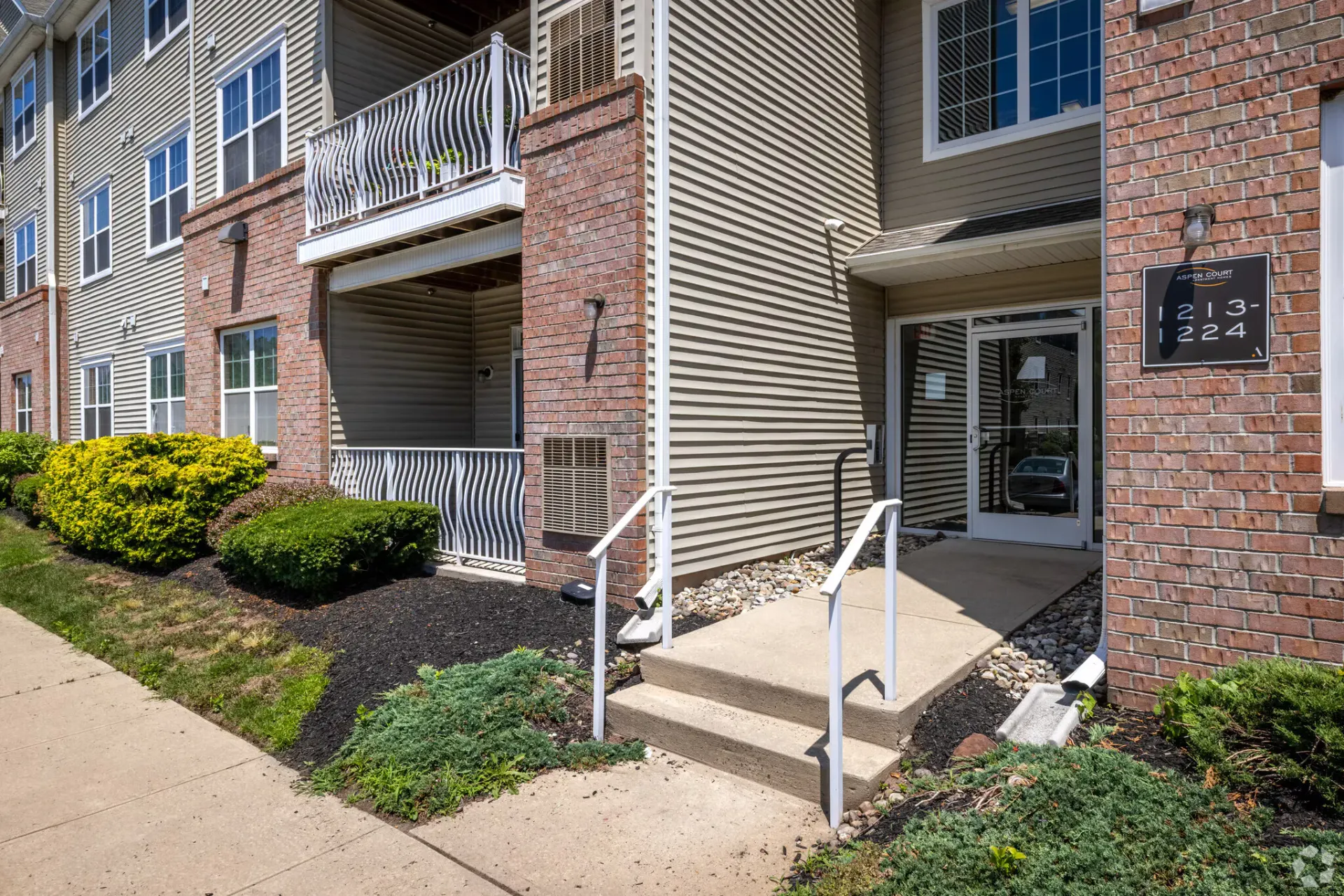Exterior entrance to a multifamily building with brick and siding, steps and handrails.
