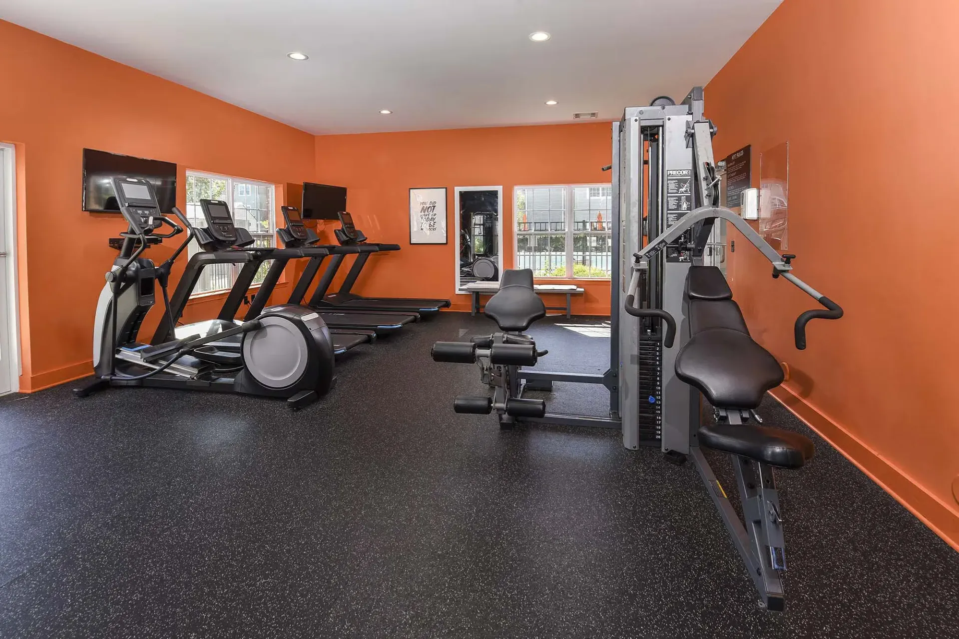 Bright orange-walled community gym with treadmills, elliptical, and weight machines.